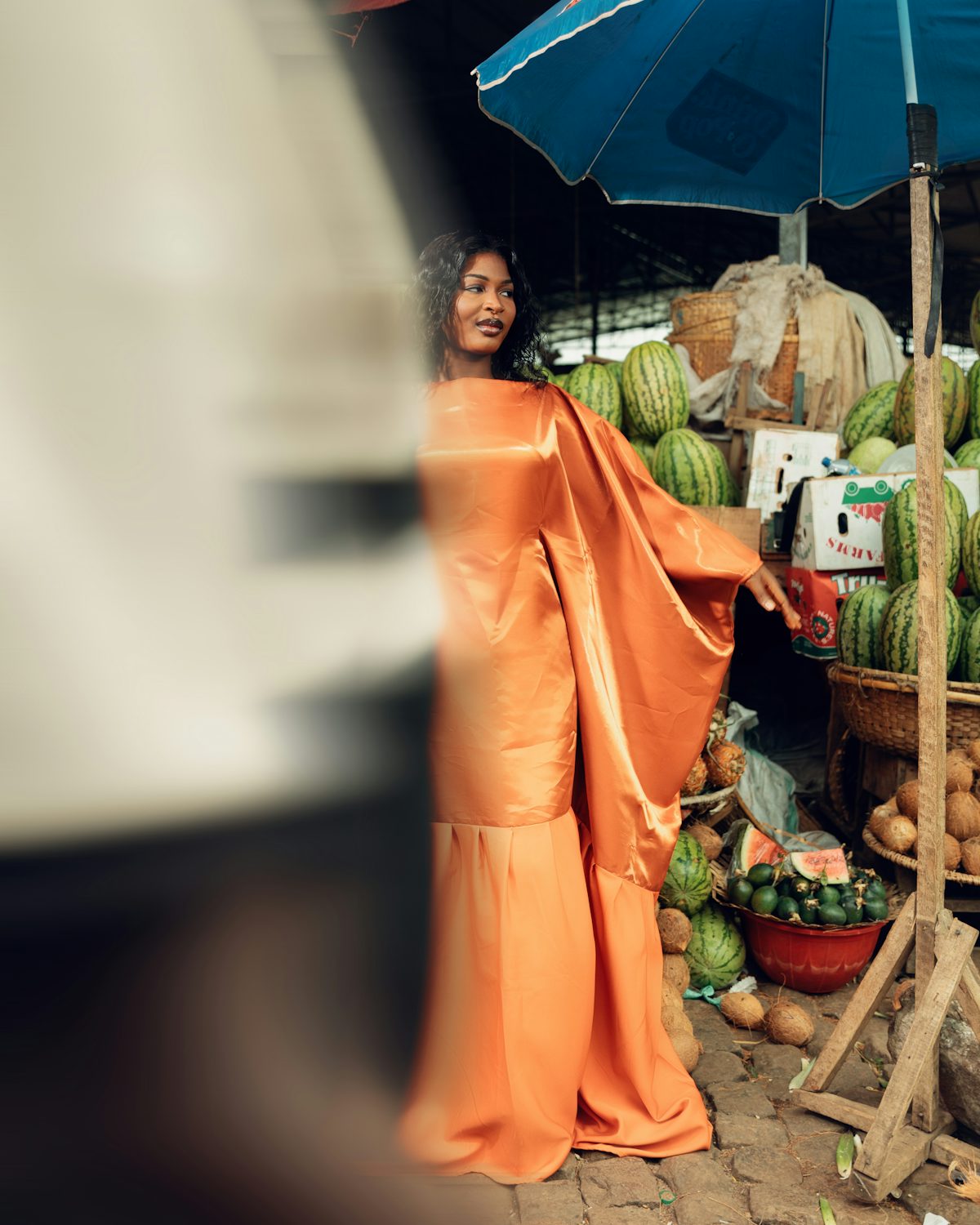 A trader in a flowing orange dress at a fruit stand
